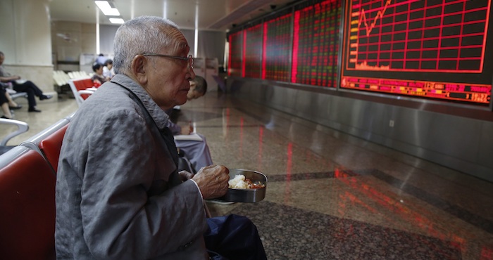 Un veterano inversionista de valores almuerza junto a una pantalla que muestra el índice de valores en la Bolsa de Valores en Pekín (China). Foto: EFE.