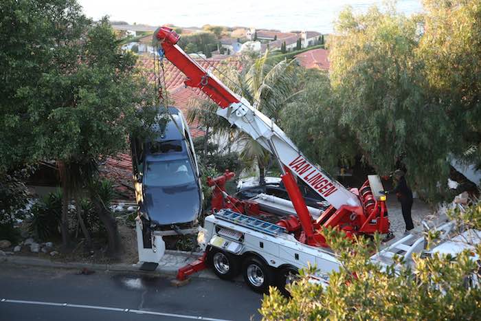 Una grúa baja al auto que se estrelló y que terminó sobre el techo de una casa en Palos Verdes Estates, California. Foto: AP.