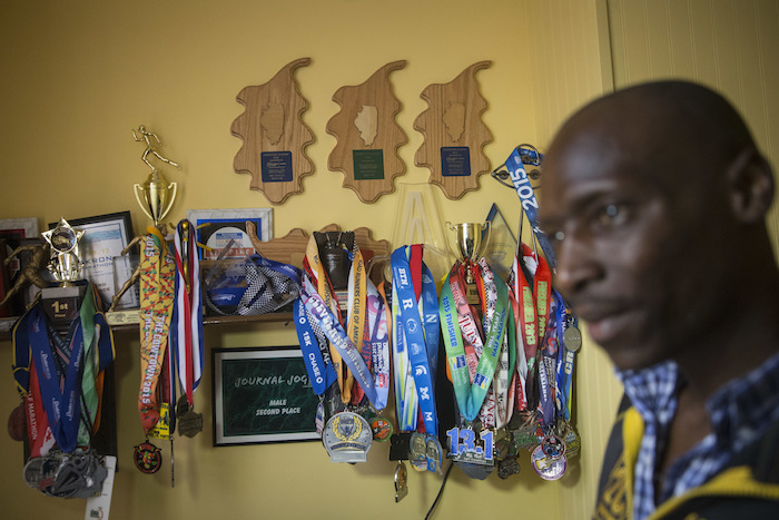 El corredor Peter Kemboi junto a un muro de trofeos ganados por los corredores que trabajan con la agente de carreras Larisa Mikhaylova, en la residencia dle grupo en Newport, Kentucky. Foto: AP