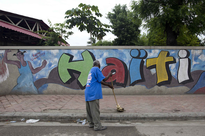 Un hombre barre una vereda frente a un muro de seguridad decorado con una imagen de una mujer bailando y la palabra "Haiti" escrita en colores brillantes, en Petion-Ville, un suburbio de Puerto Príncipe, Haití. Foto: AP