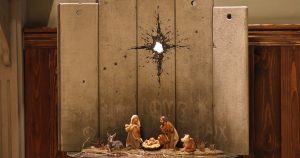 Pequeños fragmentos de muro, en los que algunas inscripciones apelan a la paz y al amor, sirven de segundo plano a un nacimiento creado sobre una pequeña mesa con regalos a sus pies. Foto: RT. 