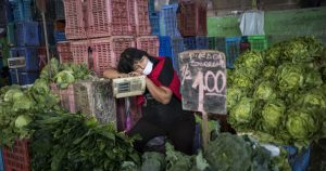 Kathy Velázquez, con una mascarilla para protegerse del coronavirus, duerme en su puesto de verduras mientras aguarda la llegada de clientes, en Lima, Perú, el sábado 11 de abril de 2020.