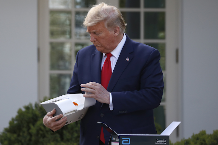 En esta imagen del 30 de marzo de 2020, el Presidente Donald Trump abre una caja que contiene una prueba de 5 minutos para detectar COVID-19 de Abbott Laboratories, mientras Stephen Hahn, comisionado de la Administración de Alimentos y Medicamentos, habla sobre el coronavirus, en la Casa Blanca, en Washington.