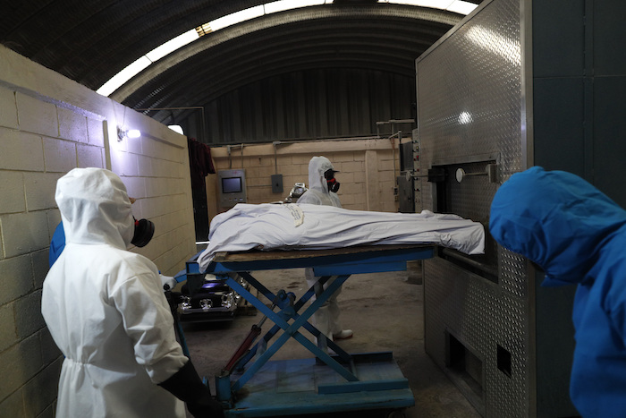 Trabajadores con equipo de protección meten a un horno el cuerpo de una persona que murió de complicaciones derivadas del coronavirus, para cremarlo, el jueves 21 de mayo de 2020 en el Mausoleo San Cristóbal en Ecatepec, México. 