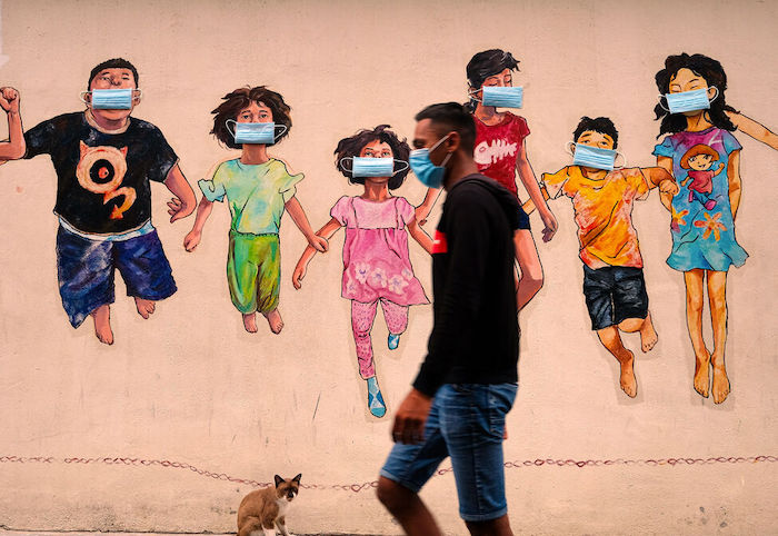 Un hombre con mascarilla camina junto a un mural en Ipoh, Malasia.