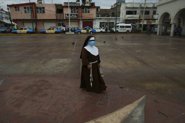 Una monja, con mascarilla en durante la pandemia de la COVID-19, camina por la plaza principal de Acatlán de Osorio, una localidad mexicana cuyo motor son las remesas que envían los residentes emigrados, el 25 de junio de 2020.
