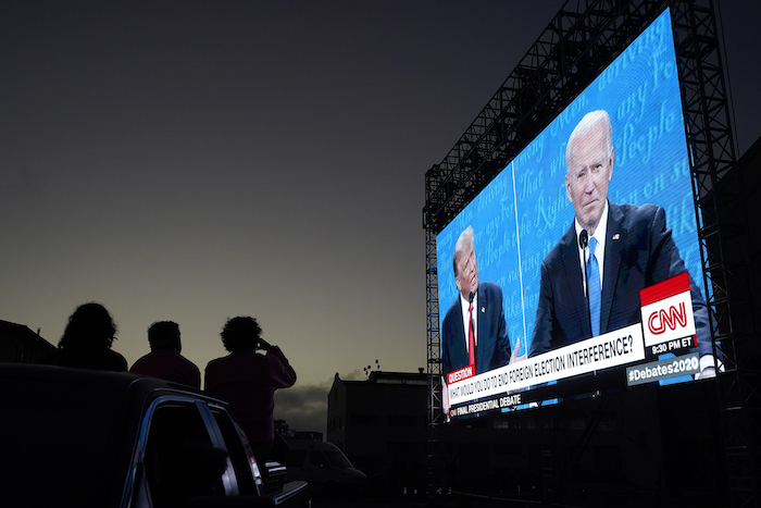 Varias personas siguen desde sus autos el debate presidencial entre el presidente, Donald Trump (a la izquierda en la pantalla), y el aspirante demócrata, Joe Biden, en Fort Mason Center, San Francisco, el 22 de octubre de 2020.