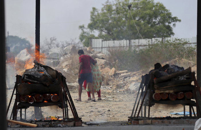 Familiares de víctimas de la COVID-19 se marchan mientras sus piras funerarias arden en un crematorio al aire libre en una cantera de granito, a las afueras de Bengaluru, India, el 5 de mayo de 2021.