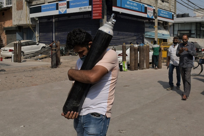 En esta imagen de archivo del 3 de mayo de 2021, un hombre camina con una botella llena de oxígeno mientras varios familiares de pacientes de COVID-19 esperan en fila para rellenar sus botellas, en la zona de Mayapuri, en Nueva Delhi, India.