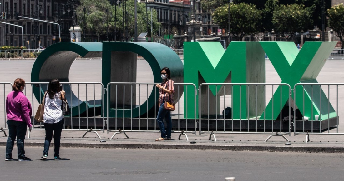 Turistas se toman una fotografía en las emblemáticas letras "CdMx" ubicadas en la Plancha del Zócalo capitalino, la cual se encuentra cercada con vallas metálicas para evitar aglomeraciones.
