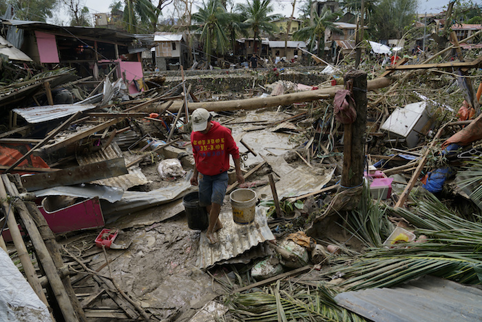 Un hombre carga cubos junto a casas dañadas por el tifón "Rai" en Talisay, en la provincia de Cebú, Filipinas, el viernes 17 de diciembre de 2021.
