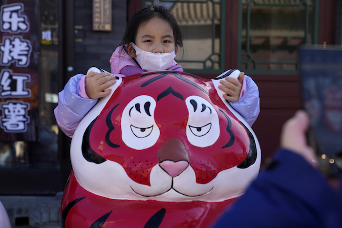 Una niña con mascarilla se agarra a las orejas de una estatua de un tigre en el primer día del Año Nuevo Lunar del Tigre, en Beijing, China, el 1 de febrero de 2022.