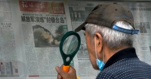 Un hombre usa una lupa para leer un periódico que informa sobre ejercicios militares de China alrededor de Taiwán, en Beijing, el 7 de agosto de 2022. Foto: Andy Wong, AP.