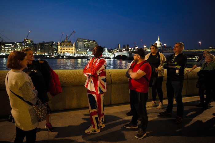 Un hombre, vestido con un traje con los colores de la bandera de Gran Bretaña, permanece de pie junto a otras personas para dar el pésame ante el ataúd de la reina Isabel II, el cual se encuentra en el Salón Westminster, el miércoles 14 de septiembre de 2022, en Londres.