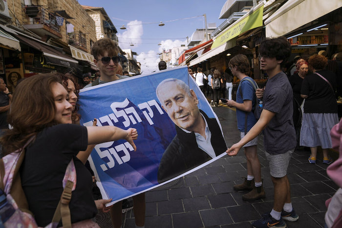 Gente haciéndose fotos con un cartel electoral que muestra al exprimer Ministro israelí y líder del partido Likud Benjamin Netanyahu, en el mercado Mahane Yehuda de Jerusalén, el día anterior a las elecciones nacionales israelíes, el lunes 31 de octubre de 2022.
