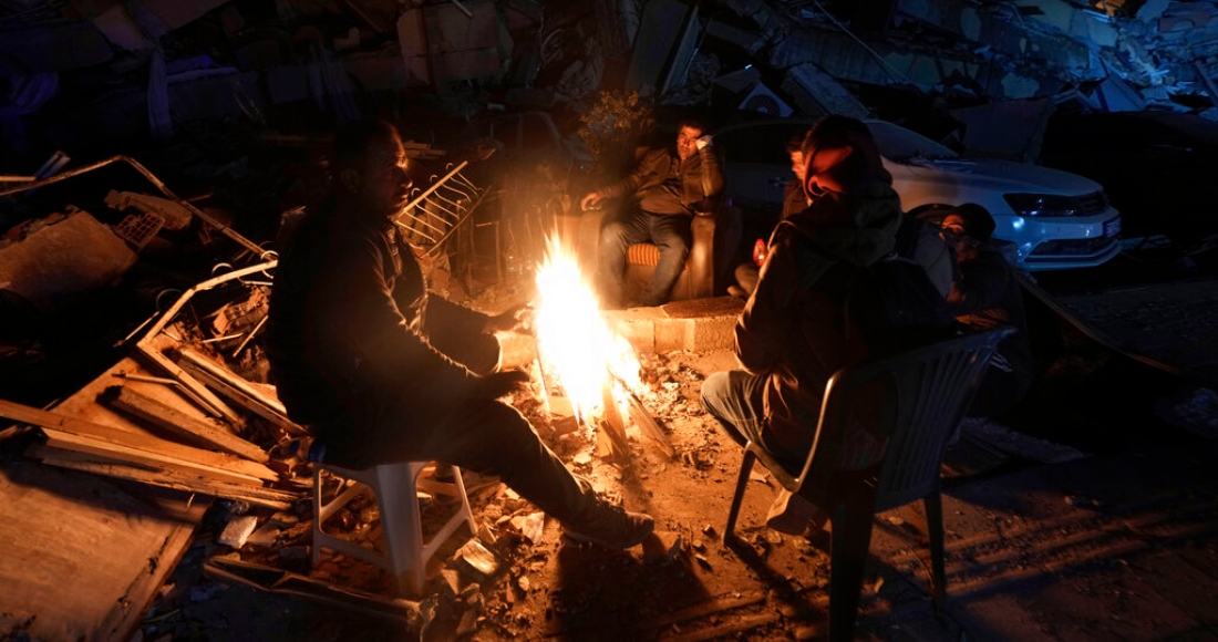 Varias personas se calientan alrededor de una hoguera delante de edificios destrozados por un potente sismo, en Antakya, en el sur de Turquía, el 8 de febrero de 2023.