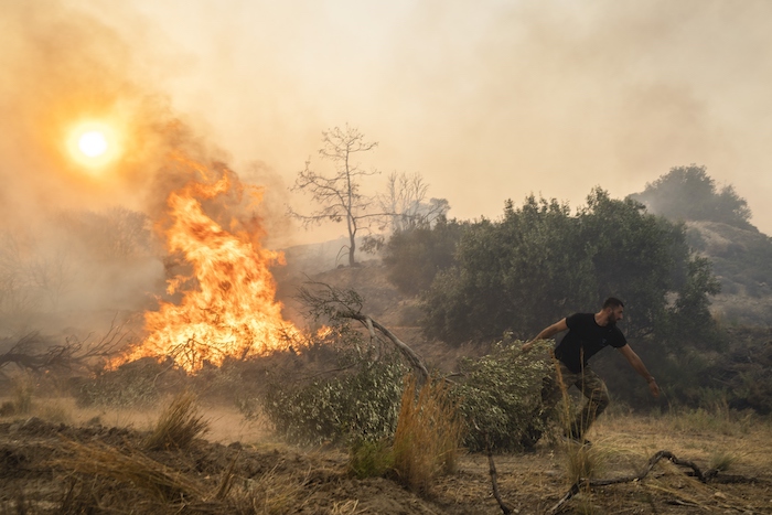 Ilias Kyriakou, de 25 años, arrastra una rama de olivo mientras un incendio quema parte de la localidad de Gennadi, en la isla de Rodas, en el sureste de Grecia, el 25 de julio de 2023.