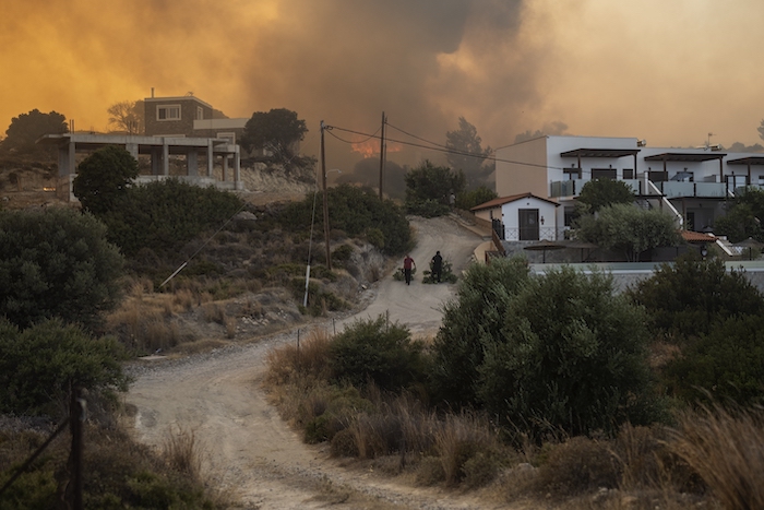 Residentes arrastran ramas de árboles mientras un incendio arde en las inmediaciones de Gennadi, en la isla de Rodas, en el sureste de Grecia, el 25 de julio de 2023.