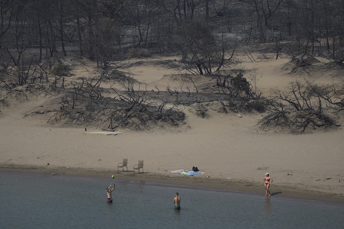 Varias personas juegan con una pelota delante de unos arbustos quemados en la playa de Glystra, cerca de Gennadi, en la isla de Rodas, en el sureste de Grecia, el 27 de julio de 2023.