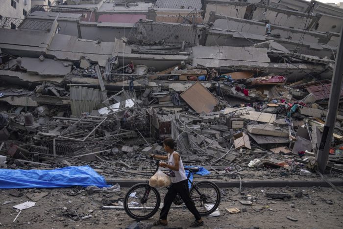 Un niño palestino camina con una bicicleta junto a los restos de un edificio alcanzado por un ataque aéreo israelí en la ciudad de Gaza, el domingo 8 de octubre de 2023.