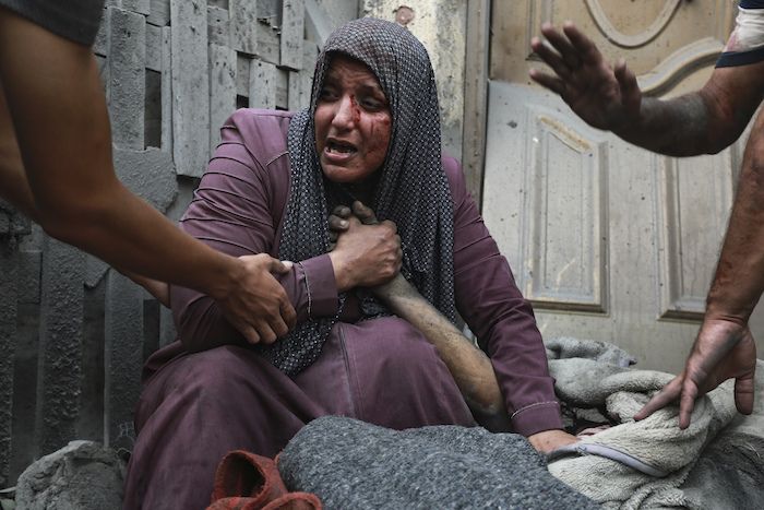 Una mujer palestina herida llora mientras sostiene la mano de su familiar muerto ante su casa tras ataques israelíes que golpearon su vecindario en Ciudad de Gaza. Foto: Abed Khaled, AP