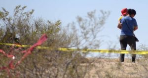 Una mujer con un niño en brazos camina sobre el terreno baldío donde se localizaron fosas clandestinas en Ciudad Juárez, en septiembre de 2023. Foto: Rey R. Jauregui, La Verdad.