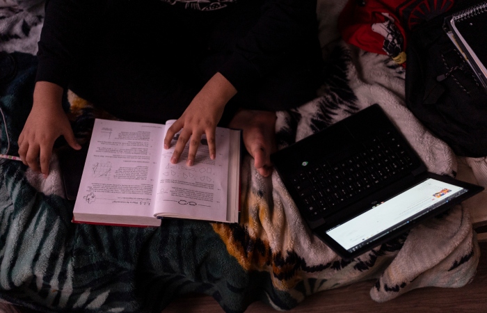 Deneffy hace su tarea en la laptop de la escuela en una litera que comparte con su madre y hermanita en un apartamento tipo estudio, donde su familia paga 700 dólares al mes a un compañero de piso para rentar el espacio.