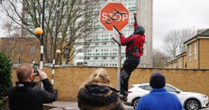 Una persona retira una obra de arte de Banksy que parece mostrar tres drones sobre un cartel de Stop que fue develado en la intersección de las calles Southampton Way y Commercial Way en Peckham, sureste de Londres, viernes 22 de diciembre de 2023. (Aaron Chown/PA via AP)