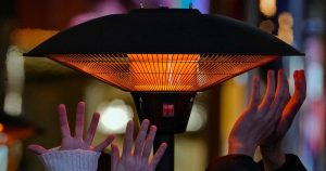Gente tratando de calentarse las manos con un calefactor mientras esperan a su mesa ante una restaurante en un centro comercial al aire libre en Beijing, el sábado 23 de diciembre de 2023. (AP Foto/Andy Wong)
