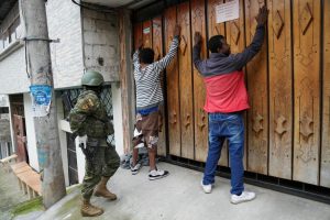 Dos personas contra una puerta con las manos en alto y un militar procede a registrarlos mientras patrullan por el sur de Quito, Ecuador, el viernes 12 de enero de 2024, como secuela a la fuga de dos cabecillas de bandas criminales de prisión.