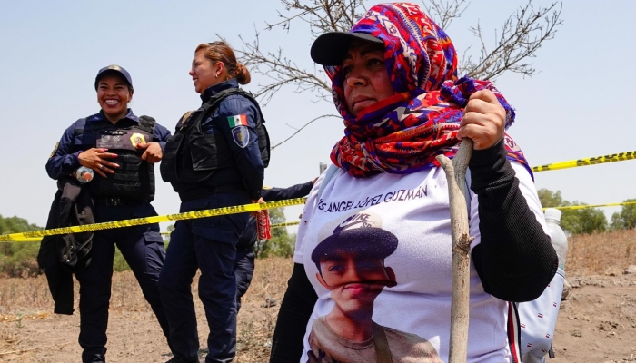Buscadora observa predio en el que Ceci Flores había señalado que se encontraron restos humanos y un supuesto crematorio clandestino, mientras policías a sus espaldas rien.