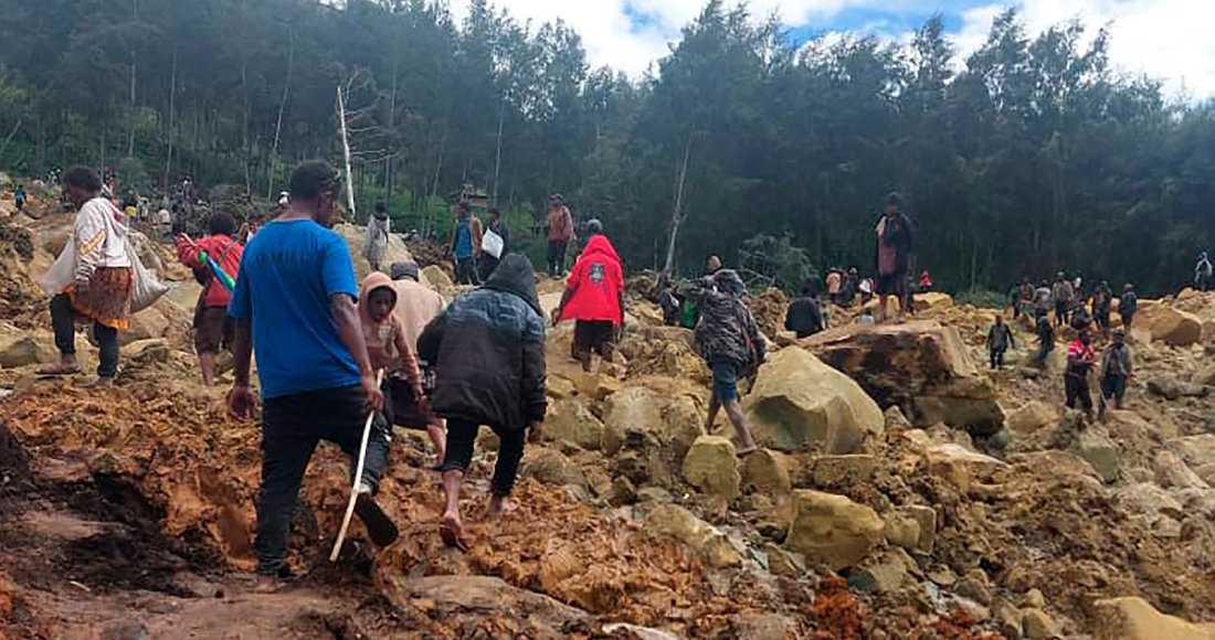 En esta imagen proporcionada por la Organización Internacional para las Migraciones, un grupo de personas cruza un área afectada por un deslave para llevar a la otra área de la aldea de Yambali, en Papúa Nueva Guinea, el viernes 24 de mayo de 2024.
