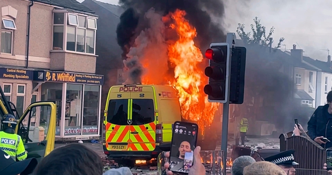 Una camioneta de la policía arde mientras una multitud choca con la policía el martes 30 de julio de 2024 en Southport, en el noroeste de Inglaterra, cerca de donde tres niñas murieron apuñaladas en una clase de danza el día anterior. La violencia estalló poco después de una vigilia pacífica a la que asistieron cientos de personas en el centro de Southport en gesto de duelo por las víctimas.