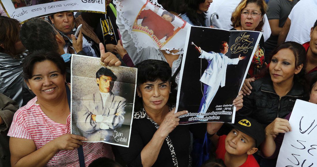 Admiradores sostienen afiches del cantante mientras esperan para rendirle sus últimos honores. Foto: AP